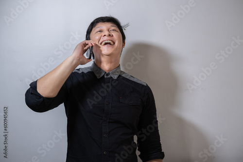 Adult Asian man wearing black shirt is calling with smiling and happy expression photo