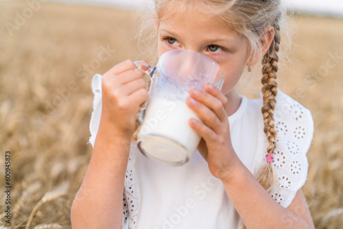 little blonde girl with pigtails in a rye field with a mug of milk  the concept of healthy eating  eco friendly farm products