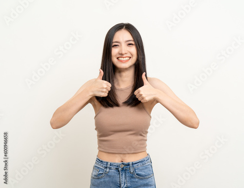 Beautiful smiling happy young asian woman age around 25 in brown shirt. Charming female lady showing thumbs up on isolated background. Asian cute people looking camera confident with white backdrop.