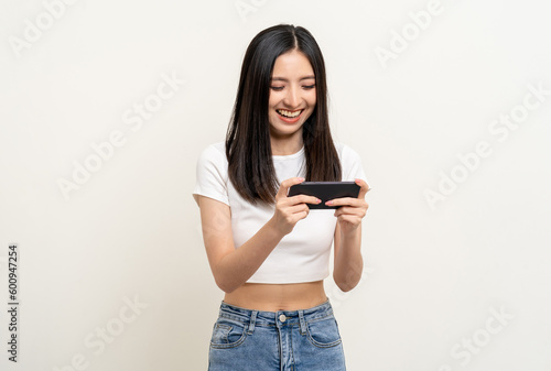 Excited Beautiful young asian women play mobile game and standing on isolated white background. Playing game on smartphone winning victory moment. Very enjoy and fun relax time