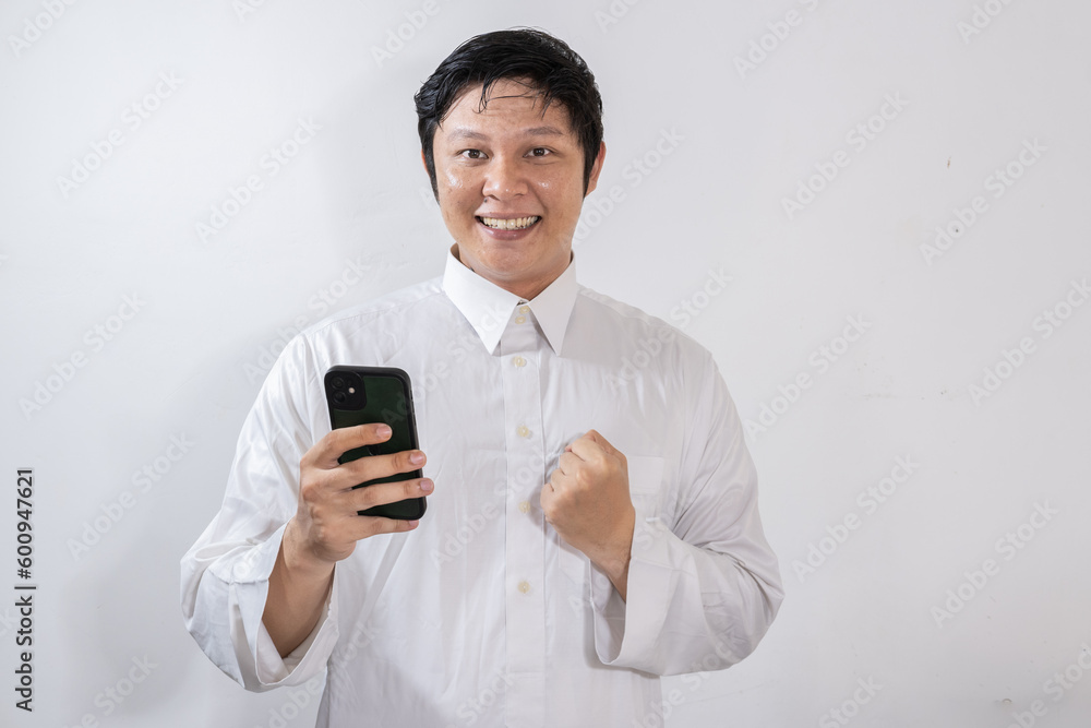 Happy looking Asian Muslim man showing joy while looking at his mobile phone Happy looking Asian Muslim man showing joy while looking at his mobile phone