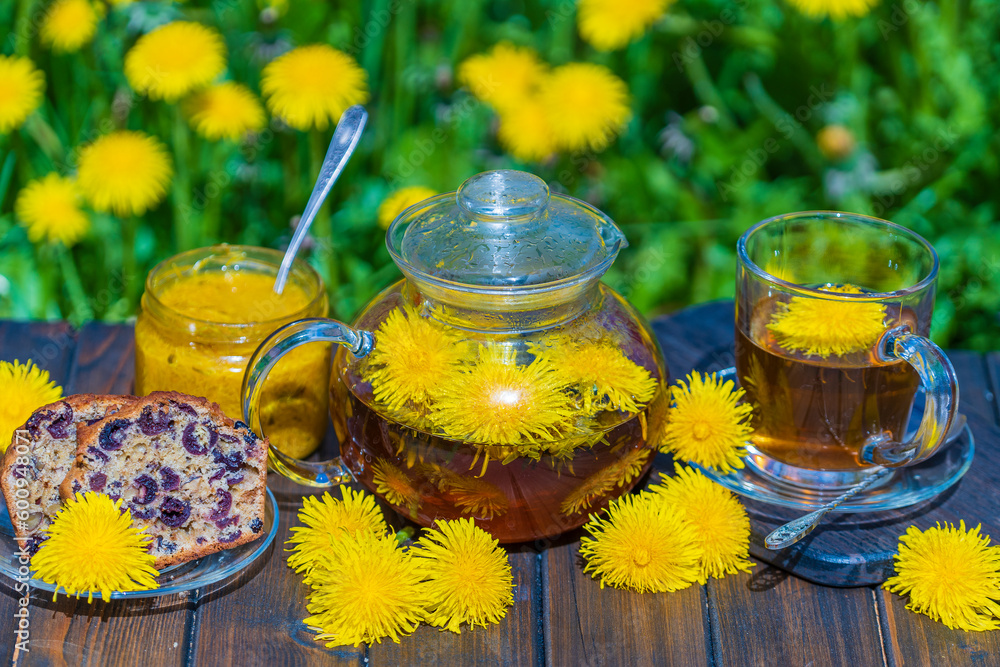 Healthy dandelion flower tea in a glass teapot on the wooden table along with sweet jam and cherry muffin in the spring garden, closeup Healthy dandelion flower tea in a glass teapot on the wooden table along with sweet jam and cherry muffin in the spring garden, closeup