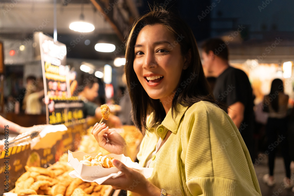 Naklejka premium Asian woman enjoy eating fries street food at night market. Traveler Asian blogger women Happy tourists Beautiful female with Traditional thailand bangkok food.