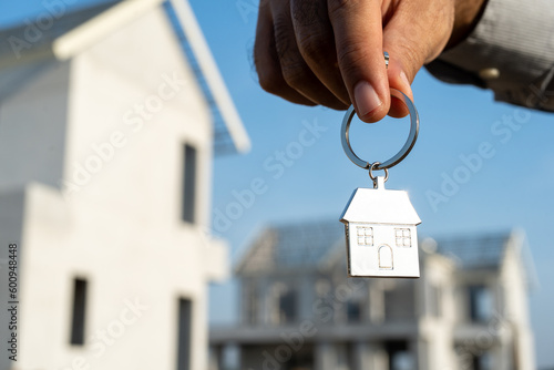 Close up male hand holding house key with sunlight. Real estate agent at construction site. New home purchase sales or rent. Choose Planning to buy property