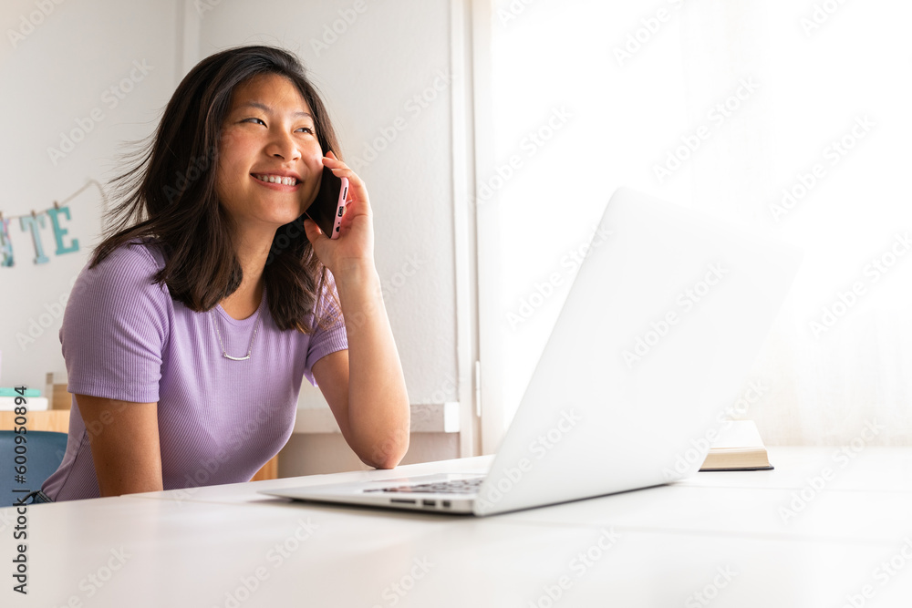 Happy Asian woman smiling talking on the phone while working at home office. College student using mobile phone. Happy Asian woman smiling talking on the phone while working at home office. College student using mobile phone.