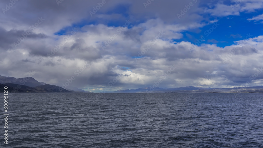 Ripples on the blue water of the Beagle Canal. In the distance, against the background of the azure sky and clouds - a mountain range. Argentina. Tierra del Fuego Archipelago.