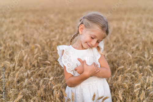 little blonde girl with pigtails in a rye field with a mug of milk, the concept of healthy eating, eco friendly farm products