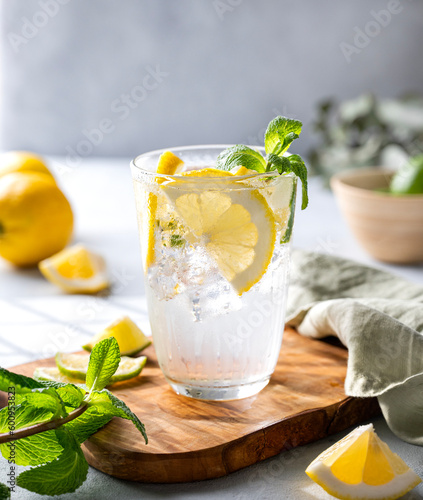 Lemonade drink with fresh lemons, lime, mint and ice. Refreshing citrus mojito cocktail on a light background with shadow. Summer cold drinks concept. photo