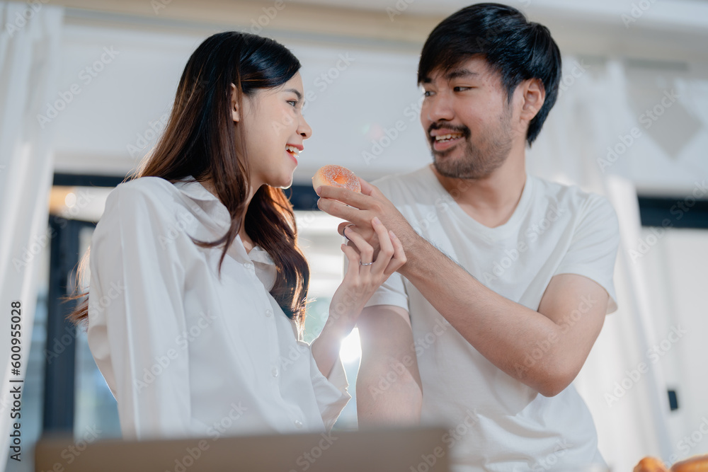 Happy young male holding donuts in hands, with smiling wife, enjoying cooking together in modern kitchen on weekend. Happy young male holding donuts in hands, with smiling wife, enjoying cooking together in modern kitchen on weekend.