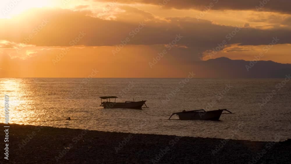 Person swimming in the ocean to moored fishing boats during beautiful golden sky sunset in capital Dili, East Timor Timor-Leste Person swimming in the ocean to moored fishing boats during beautiful golden sky sunset in capital Dili, East Timor Timor-Leste