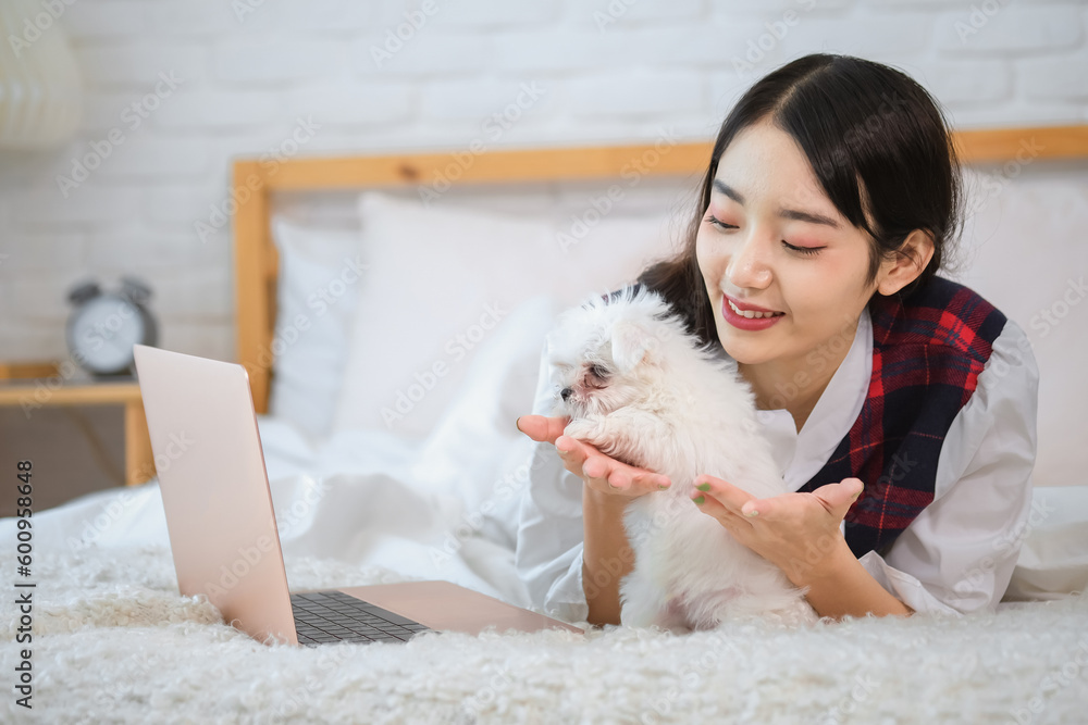 Beautiful asian owner smile uncontrollably as her cute white dog lovingly played with her hand on the bed. Beautiful asian owner smile uncontrollably as her cute white dog lovingly played with her hand on the bed.