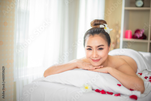 Beautiful asian woman smiling happily on a bed strewn with roses in a spa room.