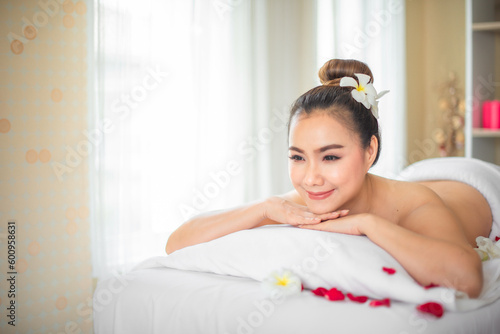Surrounded by the delicate fragrance of roses the beautiful asian woman seemed lost in a world of her own free from stress and worries on the bed strewn with roses in spa room.
