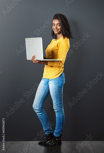 Portrait, happy indian woman standing with laptop and in wall background. Social media or networking, technology or communication and smiling African female worker with mockup in studio backdrop.