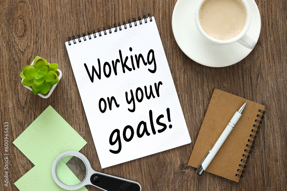 text WORKING ON YOUR GOALS on white note paper near coffee cup text WORKING ON YOUR GOALS on white note paper near coffee cup