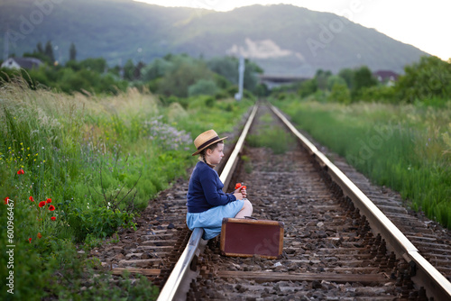 A little girl in a dress sits on an abandoned railroad tracks