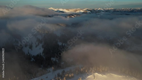 Flying Above Clouds, Mountain Hillis Covered With Snow and Pine Forest on Sunny Winter Evening, Drone Shot photo