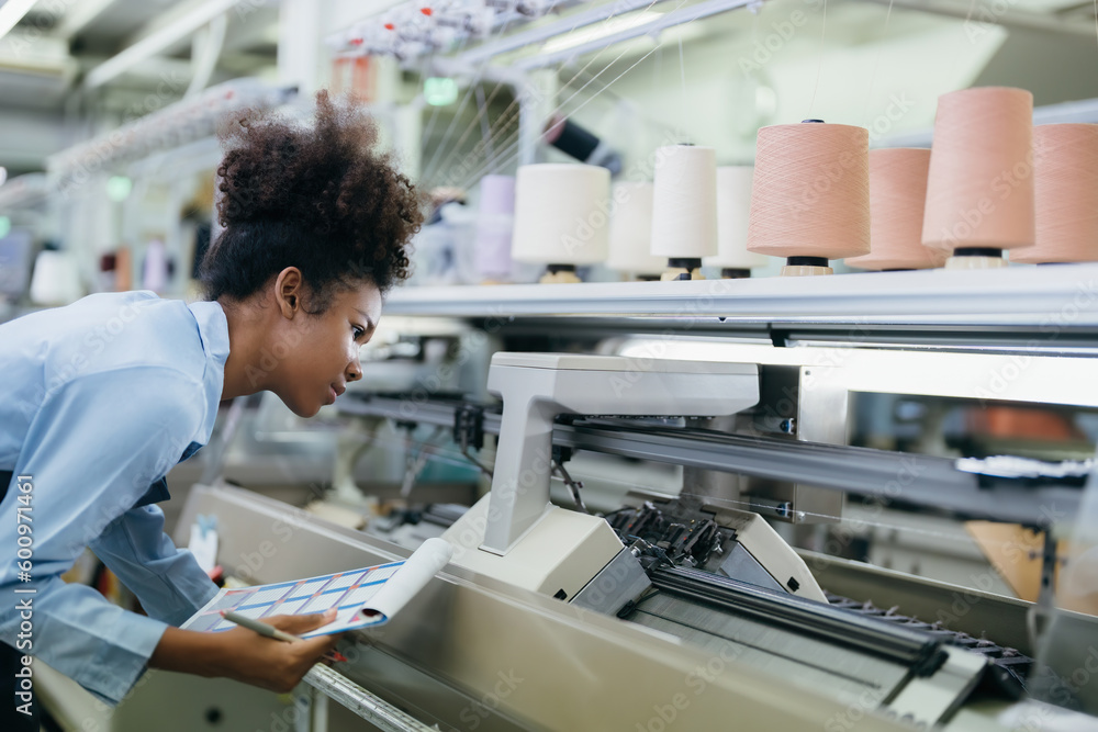 Obraz premium American seamstress designer with curly hair He was checking the weaving machine and the sewing thread attentively. wearing a uniform and carrying a catalog in the weaving industry