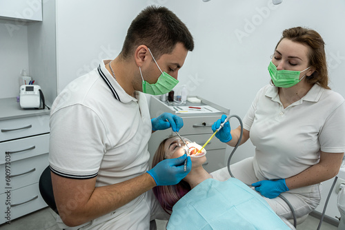 patient is lying in dentistry where she is being treated by male somatologist female assistant