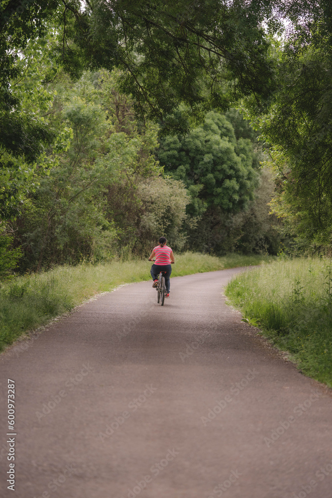 A woman in comfortable pink clothes riding a mountain bike on a road with trees on the side. A woman in comfortable pink clothes riding a mountain bike on a road with trees on the side.