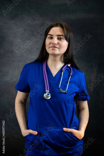 beautiful female doctor or medical student  in blue uiform with stethoscope against dark background photo