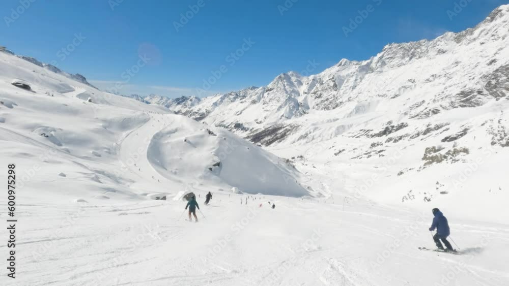 Slow motion of skiers pass by skiing fast downhill on a piste in Cervinia ski resort italian alps on a sunny day Slow motion of skiers pass by skiing fast downhill on a piste in Cervinia ski resort italian alps on a sunny day