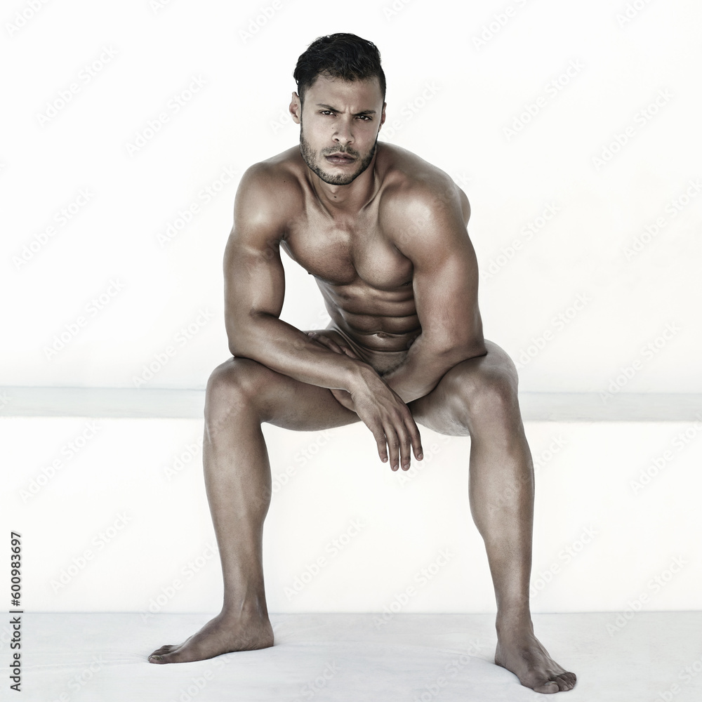 Obraz premium Nude, body and man in portrait isolated on a wall background for health, fitness and wellness. Naked, strong and face of a sexy male model sitting with muscles for power, sports and exercise results