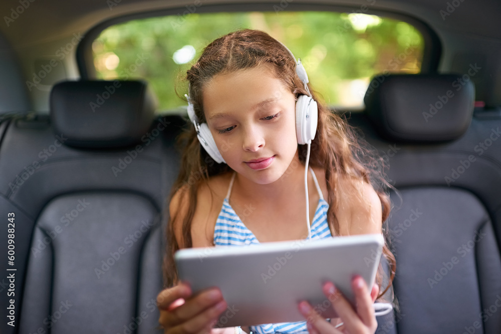 Technology, young girl in car with tablet and headphones while travelling. Social media or streaming, internet connectivity and child on road trip on vacation in vehicle with digital or mobile device