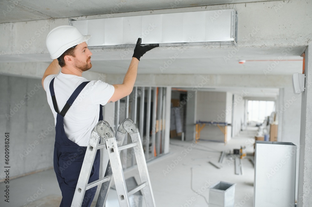 Professional HVAC Worker on a Aluminium Scaffolding Installing Air Duct Inside Newly Built Commercial Building. Industrial Theme Professional HVAC Worker on a Aluminium Scaffolding Installing Air Duct Inside Newly Built Commercial Building. Industrial Theme