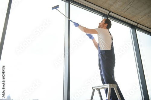 An employee of a professional cleaning service washes the glass of the windows of the building. Showcase cleaning for shops and businesses.