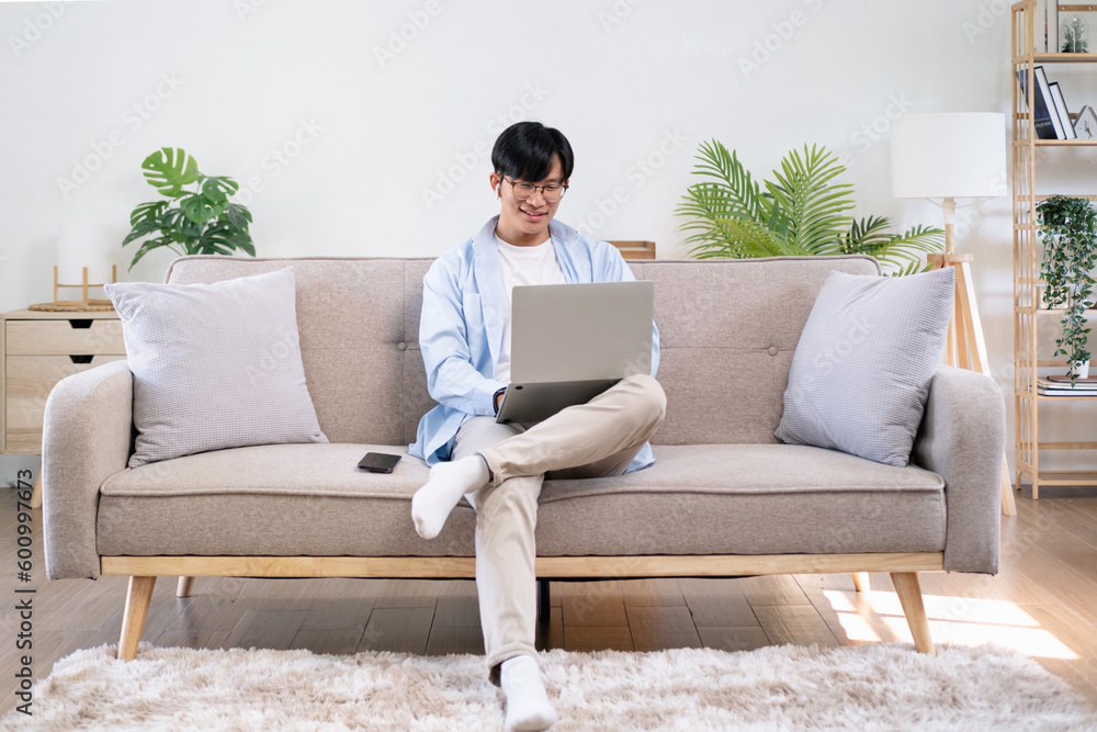 Pleasant happy man communicating in social network, searching information online. Asian man using laptop at living room, working from home, reading message with good news, looking at screen, training. Pleasant happy man communicating in social network, searching information online. Asian man using laptop at living room, working from home, reading message with good news, looking at screen, training.