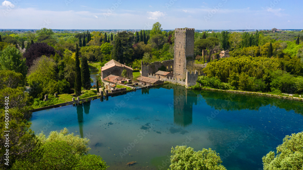 Fototapeta premium Aerial view of the ruins of the castle and tower located in the garden of Ninfa, near Latina, Italy. The park is an Italian natural monument and contains a lake and a river. It is empty.