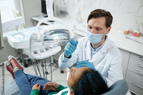 High angle view at male dentist wearing mask during child checkup in dental clinic