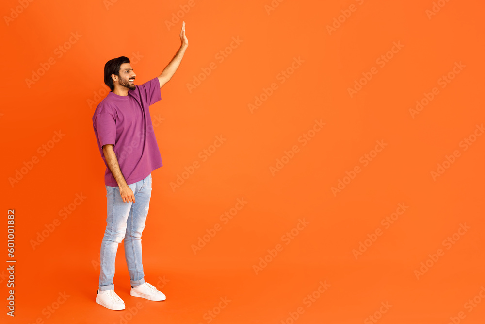 Cheerful eastern guy waving at copy space, orange background Cheerful eastern guy waving at copy space, orange background