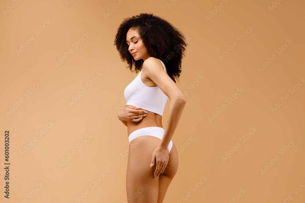 Fitness and strength. Strong and toned black woman proudly showing her well-sculpted body, posing on beige background - obrazy, fototapety, plakaty 