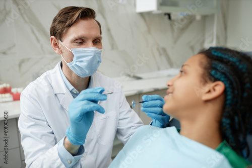Portrait of friendly male dentist wearing mask and gloves while working with teen patient in dental clinic