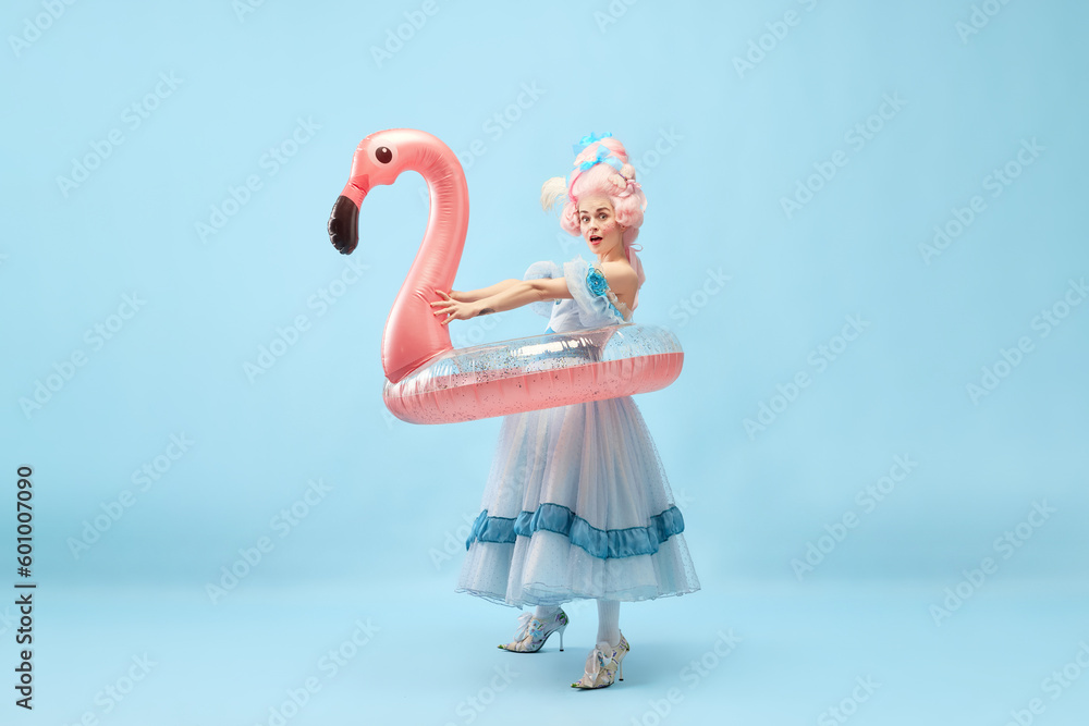 Portrait with funny beautiful princess, queen wearing dress holding pink inflatable flamingo and going beach over blue background - obrazy, fototapety, plakaty 