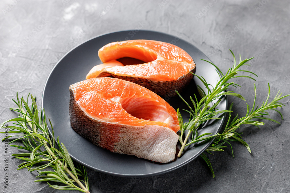 Steak of fresh raw red fish salmon with lemon, rosemary and pepper on black background Steak of fresh raw red fish salmon with lemon, rosemary and pepper on black background