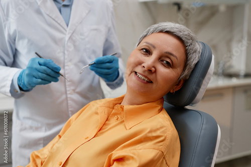 Portrait of smiling senior woman in dental clinic sitting in chair and looking at camera