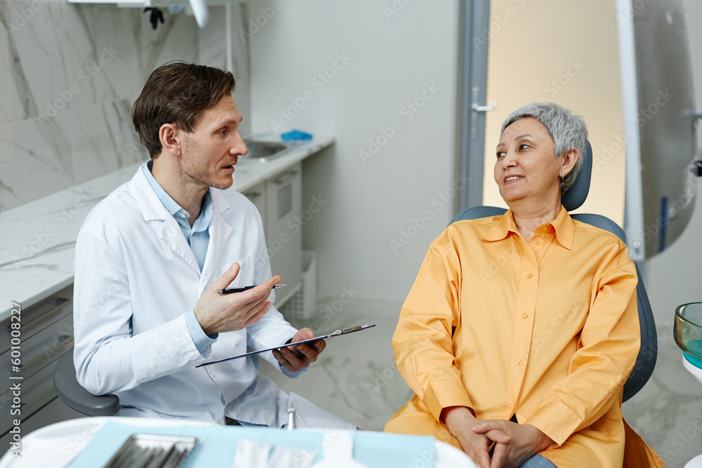 Obraz premium Side view portrait of male dentist consulting senior woman in dental clinic