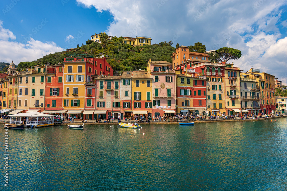 Multi coloured houses and port of Portofino, luxury tourist resort in Genoa Province, Liguria, Italy, Europe. Waterfront and promenade with many tourists on a sunny spring day. Mediterranean sea.
