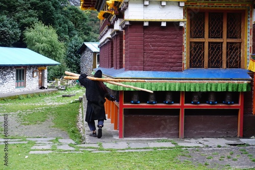 A devoted pilgrim performs Tibetan circumambulation at Hinang monastery, carrying two long logs with grace and reverence after his day's work, seeking spiritual solace in this sacred space.