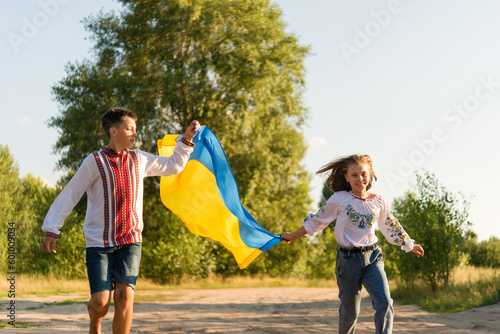 Ukrainian children girl and boy wearing national clothes with embroidery and wreath of flowers holding flag of Ukraine outdoor. Ukraines Independence, Flag Day, Constitution day. photo