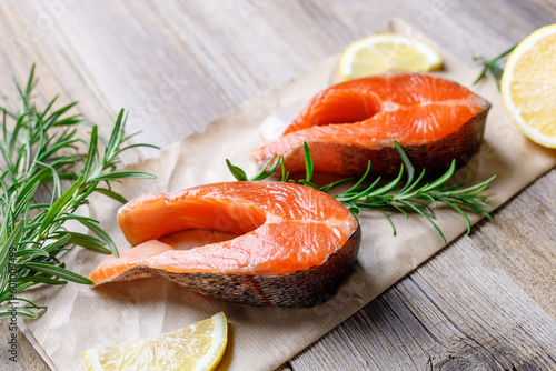 Steak of fresh raw red fish salmon with lemon, rosemary and pepper on wooden background