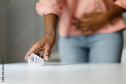 Eco-friendly menstruation revolution. Unrecognizable black lady taking menstrual cup from table  suffering from pain