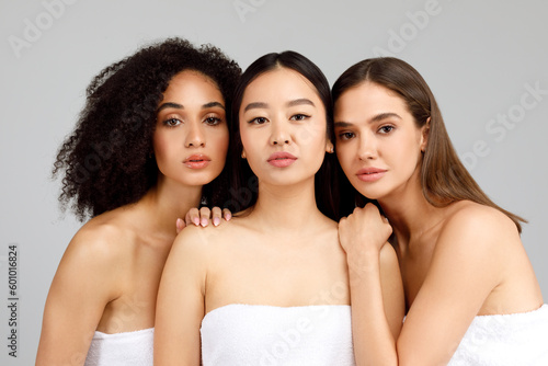 Portrait of young three multicultural ladies in bath towels posing in studio on grey background