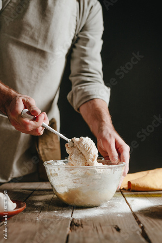 Unrecognizable man in an apron kneading the dough with a spoon