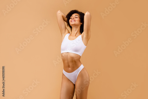 Slender young black woman posing in white underwear with hands behind her head, showing her fit strength body