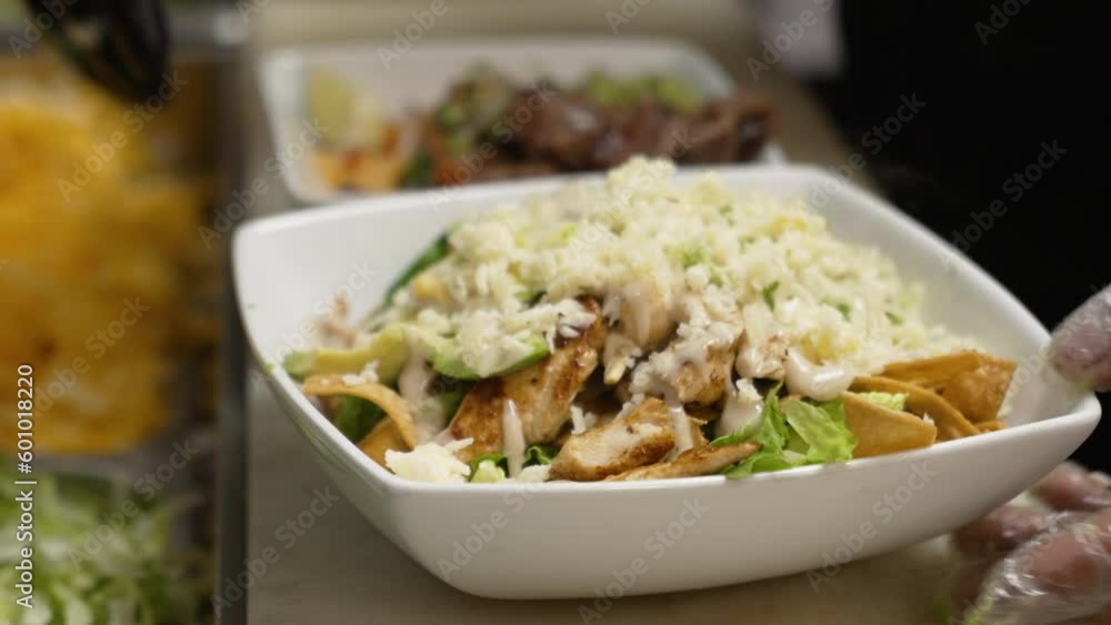 Cook tops off chicken fajita salad with shredded cheese, gloved hand sprinkles cheese to finish salad, close up slow motion 4K Cook tops off chicken fajita salad with shredded cheese, gloved hand sprinkles cheese to finish salad, close up slow motion 4K