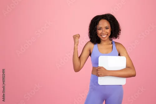 Obraz Glad millennial african american lady in sportswear hold scales, making victory sign with hand